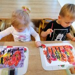 Dzieci siedzą przy stoliku, malują tło farbami akwarelowymi .jpg