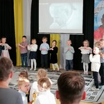Dzieci z grupy 2 występują przez zebraną publicznością. W tle na ekranie i  na banerze widać sylwetkę Papieża Jana Pawła II. jpg