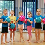 Na zdjęciu mała grupa  dzieci w strojach gimnastycznych stoi i trzyma piłki .jpg