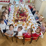 Wigilia w grupie III - Dzieci siedzą przy stole wigilijnym i uśmiechają się do zdjęcia.