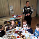 Zdjęcie przedstawia P. Dyrektor oraz  dzieci siedzące za stołem i jedzące potrawy przyniesione z domu na przedszkolną wigilię.